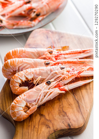 Scampi langoustine on cutting board on white table. Scampi langoustine on cutting board on white table. 129270290