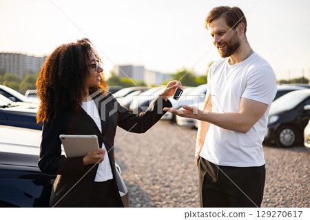 A female car dealer hands the keys to a new car to a male customer, concluding the sale. A female car dealer hands the keys to a new car to a male customer, concluding the sale. 129270617