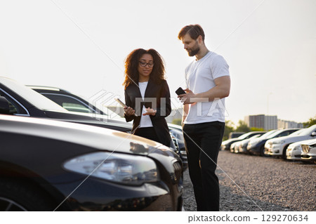 A female car dealer is showing a car to a man, discussing details and options. A female car dealer is showing a car to a man, discussing details and options. 129270634