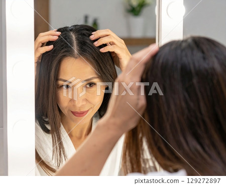 一位擔心頭髮稀疏的女性，照鏡子時摸了摸自己的髮線 129272897