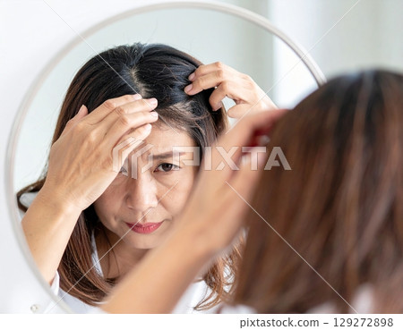 A woman who is concerned about thinning hair and touches her hairline while looking in the mirror 129272898