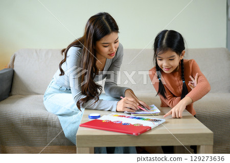 Mother and daughter enjoying art activity together at home, coloring with pencils on the table Mother and daughter enjoying art activity together at home, coloring with pencils on the table 129273636