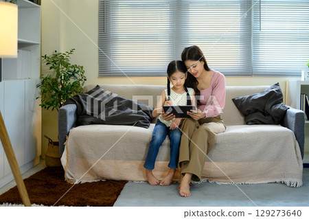 Mother and daughter sitting on a sofa using a digital tablet together in a cozy living room Mother and daughter sitting on a sofa using a digital tablet together in a cozy living room 129273640