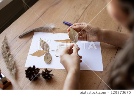 Person Crafting With Leaves and Paper on Wooden Table 129273670