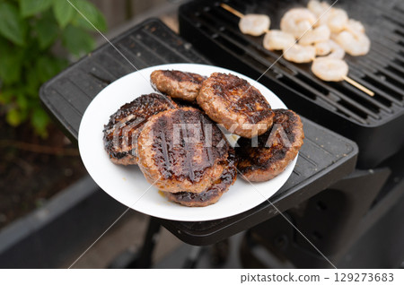 Grilled hamburgers on plate and shrimp on skewer at backyard barbecue Grilled hamburgers on plate and shrimp on skewer at backyard barbecue 129273683