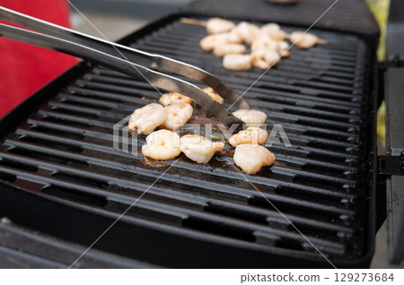 Grilled shrimp being cooked on barbecue grill with tongs Grilled shrimp being cooked on barbecue grill with tongs 129273684