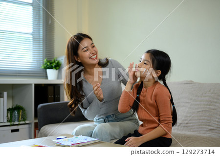 Mom and cute girl having fun with skincare routine, applying moisturizer in a living room Mom and cute girl having fun with skincare routine, applying moisturizer in a living room 129273714