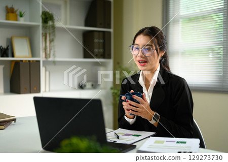 Smiling female worker holding a coffee cup while having an online meeting on a laptop 129273730