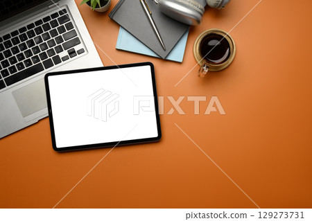 Flat lay of digital tablet, laptop, coffee cup, headphones, and stationery on orange background 129273731