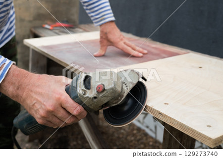 Caucasian male using angle grinder to cut wood on workbench Caucasian male using angle grinder to cut wood on workbench 129273740