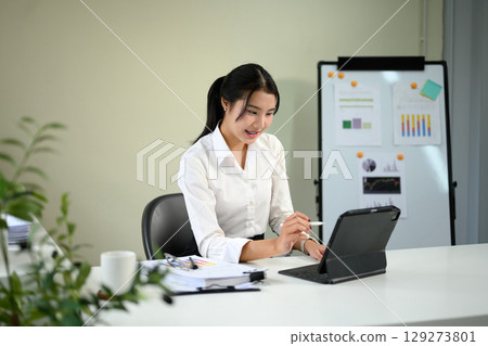 Smiling asian employee working on digital tablet at a modern office desk 129273801