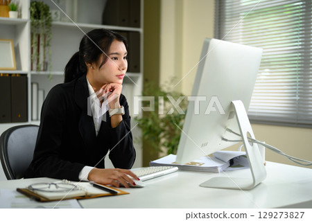Focused businesswoman working on a desktop computer in a modern office Focused businesswoman working on a desktop computer in a modern office 129273827