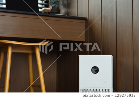 Modern air purifier placed near a wooden desk and chair in a cozy home. Healthy living concept Modern air purifier placed near a wooden desk and chair in a cozy home. Healthy living concept 129273932