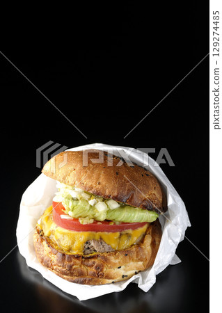 A hamburger packed with cheddar cheese photographed against a black background 129274485