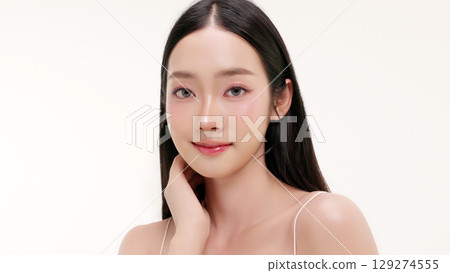 Skincare commercial of featuring a young Asian woman applying natural cosmetic cream in a soft, minimal studio setting. Ideal for promoting beauty, self-care, and organic skincare products. 129274555