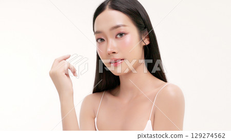 Skincare commercial of featuring a young Asian woman applying natural cosmetic cream in a soft, minimal studio setting. Ideal for promoting beauty, self-care, and organic skincare products. 129274562