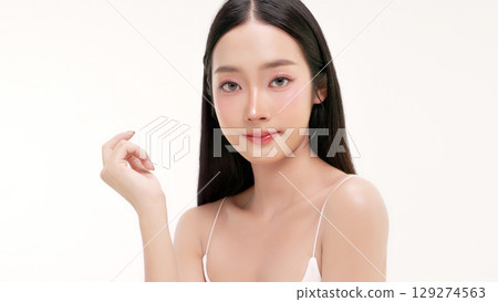 Skincare commercial of featuring a young Asian woman applying natural cosmetic cream in a soft, minimal studio setting. Ideal for promoting beauty, self-care, and organic skincare products. 129274563