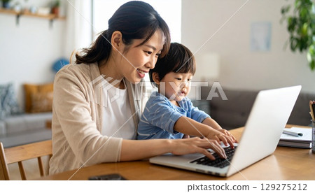 A mother working remotely while looking at a computer with her child A mother working remotely while looking at a computer with her child 129275212