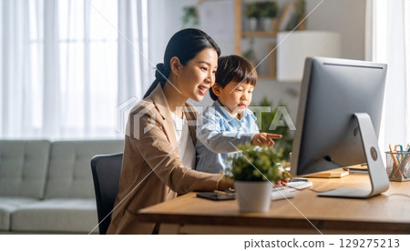 A mother working remotely while looking at a computer with her child A mother working remotely while looking at a computer with her child 129275213