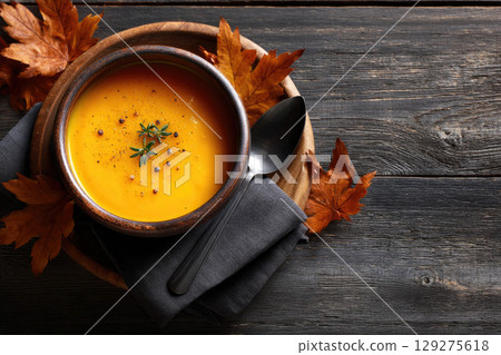 pumpkin soup in white bowl with roasted seeds and herbs on black background 129275618
