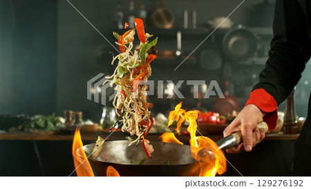 flying fresh ingredients in wok pan with whipping flames 129276192