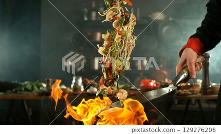 flying fresh ingredients in wok pan with whipping flames 129276208