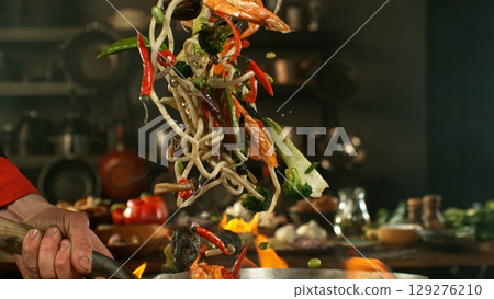 flying fresh ingredients in wok pan with whipping flames 129276210