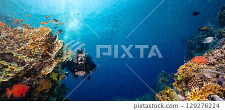 Scuba Diver Swimming in Deep Sea with Sunrays and Beautiful Coral Reef with Colorful Fishes 129276224