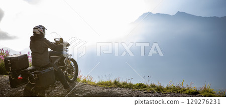 Motorcycle rider in Italian Alps during sunrise, dramatic sky. Travel and freedom, outdoor activities 129276231