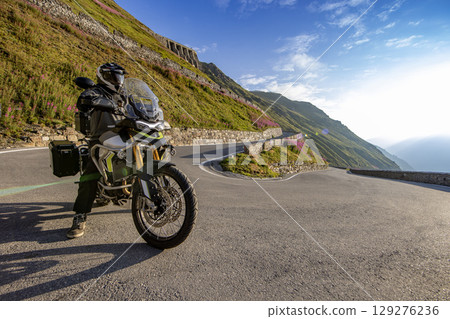 Motorcycle rider riding in Italian Alps during sunrise, dramatic sky. Travel and freedom, outdoor activities 129276236