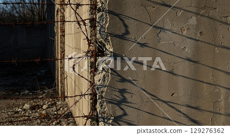 Barbed wire casts long shadow on decaying concrete wall, a stark symbol of historical sorrow 129276362