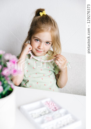 Young girl creating jewelry with colorful beads while sitting at a table indoors Young girl creating jewelry with colorful beads while sitting at a table indoors 129276373