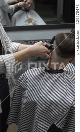 Professional barber grooming client's hair using electric clipper, delivering precise cut with skill in contemporary salon setting Professional barber grooming client's hair using electric clipper, delivering precise cut with skill in contemporary salon setting 129278478