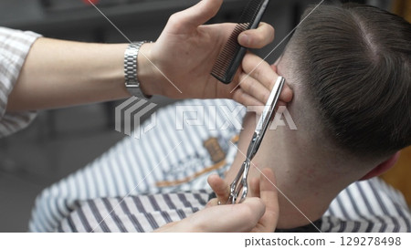 Professional barber cutting client's hair with scissors and comb, creating a stylish fade in a modern barbershop, providing a high quality grooming service Professional barber cutting client's hair with scissors and comb, creating a stylish fade in a modern barbershop, providing a high quality grooming service 129278498