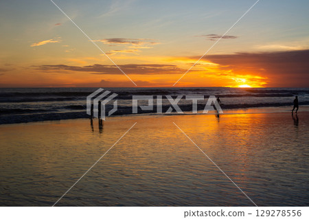 surfers catch a wave on the seashore at sunset 129278556