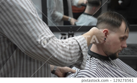 Professional barber trimming customer's hair with electric clipper, focusing on precise nape grooming within contemporary barbershop interior design 129278561