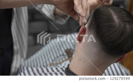 Professional barber cutting client's hair with scissors and comb, creating a stylish fade in a modern barbershop, providing a high quality grooming service 129278599