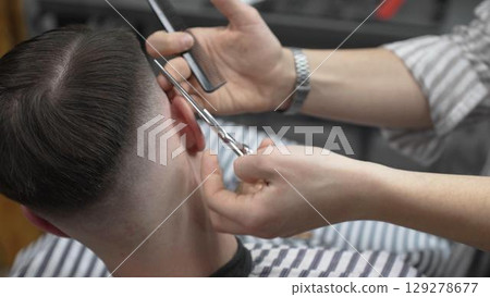 Professional barber cutting client's hair with scissors and comb, creating a stylish fade in a modern barbershop, providing a high quality grooming service Professional barber cutting client's hair with scissors and comb, creating a stylish fade in a modern barbershop, providing a high quality grooming service 129278677
