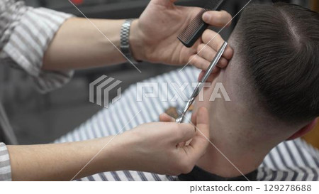 Professional barber cutting client's hair with scissors and comb, creating a stylish fade in a modern barbershop, providing a high quality grooming service 129278688
