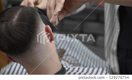 Professional barber cutting client's hair with scissors and comb, creating a stylish fade in a modern barbershop, providing a high quality grooming service Professional barber cutting client's hair with scissors and comb, creating a stylish fade in a modern barbershop, providing a high quality grooming service 129278734