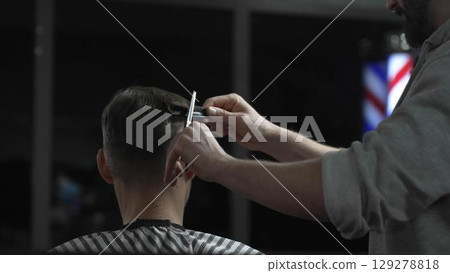 Professional barber trimming client's hair with precision scissors, creating polished hairstyle in contemporary grooming space 129278818