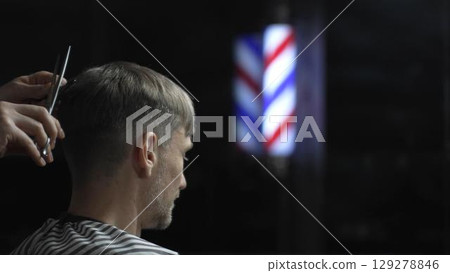 Professional barber grooming male client's hair with scissors, vintage barber pole framing traditional barbershop setting Professional barber grooming male client's hair with scissors, vintage barber pole framing traditional barbershop setting 129278846