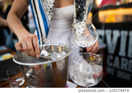 the bartender prepares an alcoholic cocktail by pouring ice cubes into a glass the bartender prepares an alcoholic cocktail by pouring ice cubes into a glass 129279479