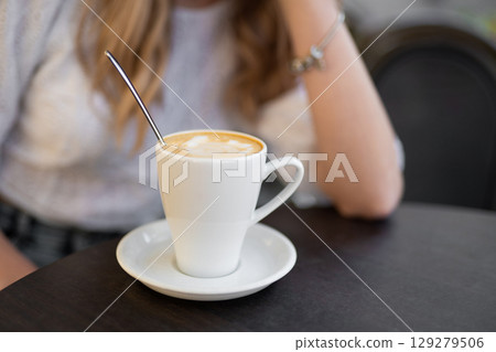 close-up of a girl's hand holding a cup of coffee at a table in a cafe close-up of a girl's hand holding a cup of coffee at a table in a cafe 129279506