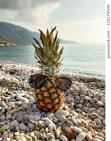 close up of a beautiful fresh pineapple on the beach wearing sunglasses 129279598