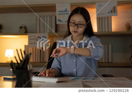 Time Management. Woman checking her watch while working on a data report. 129280226