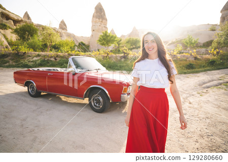 beautiful happy girl in a skirt posing near a retro car in the mountains of cappadocia 129280660
