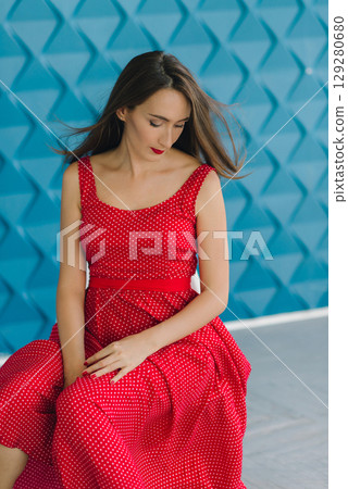 beautiful sexy girl in a red dress posing on the background of a wall in a photo studio 129280680