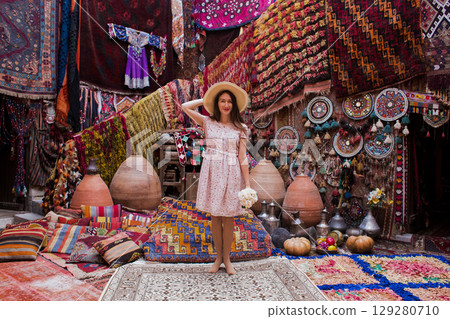 a beautiful girl in dress in a traditional turkish interior with many carpets on the wall 129280710