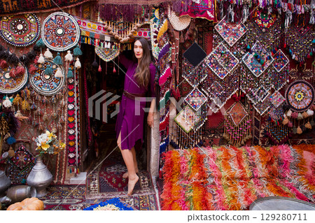 a beautiful girl in dress in a traditional turkish interior with many carpets on the wall 129280711